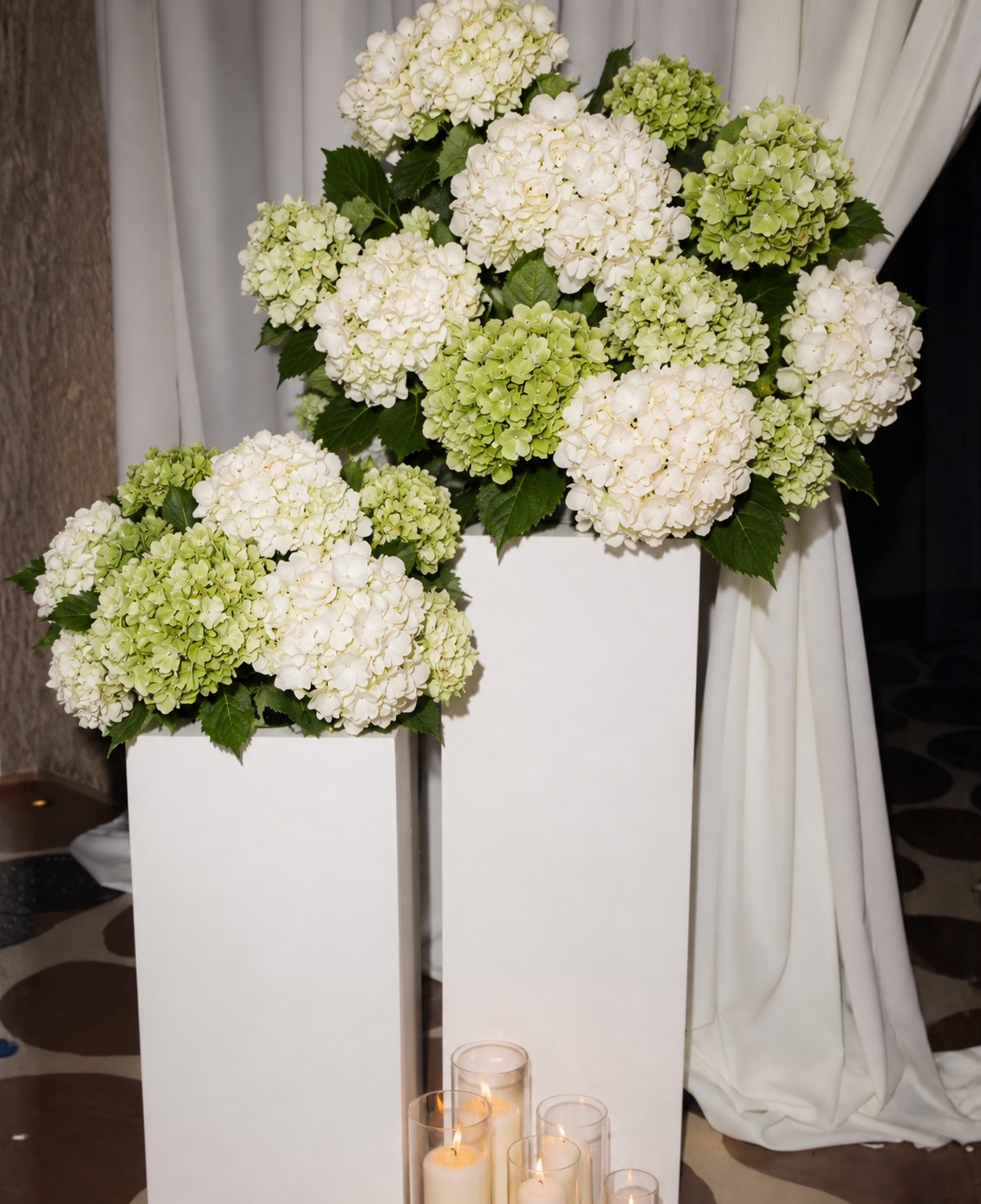 White and green hydrangeas displayed on white pedestals at the engagement party