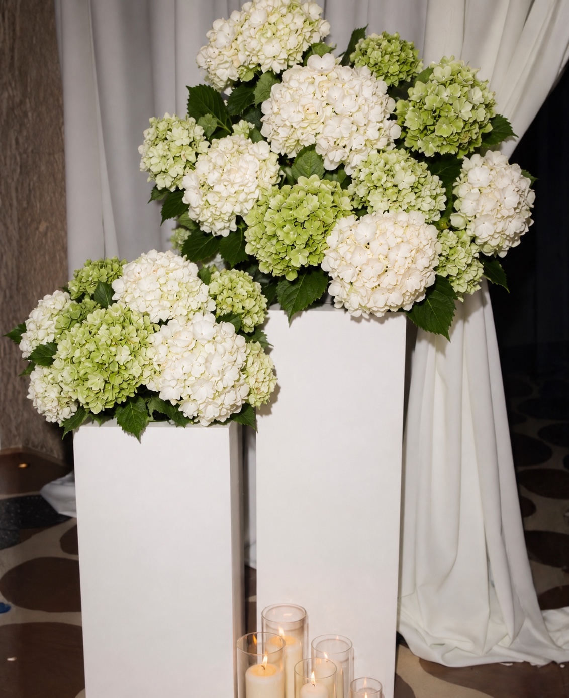White and green hydrangeas on white pedestals with glass candles at the Morgan Stanley Roccki Group Spring Soiree